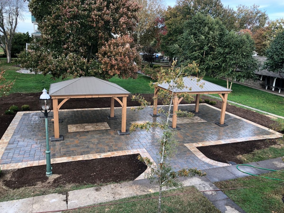 Two wooden gazebos in a landscaped park with paved paths and flower beds