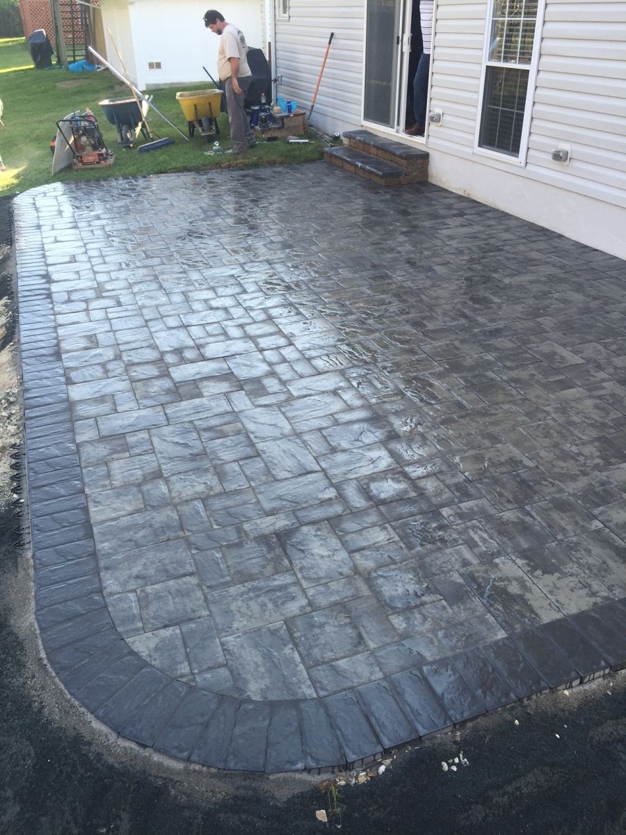 Freshly paved stamped concrete patio beside a white house, with workers in the background.