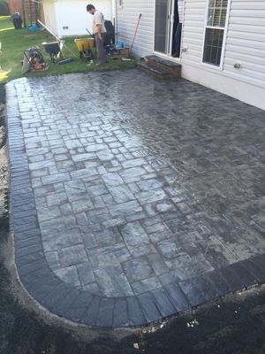 Freshly paved stone patio beside a house, with workers and tools in the yard.