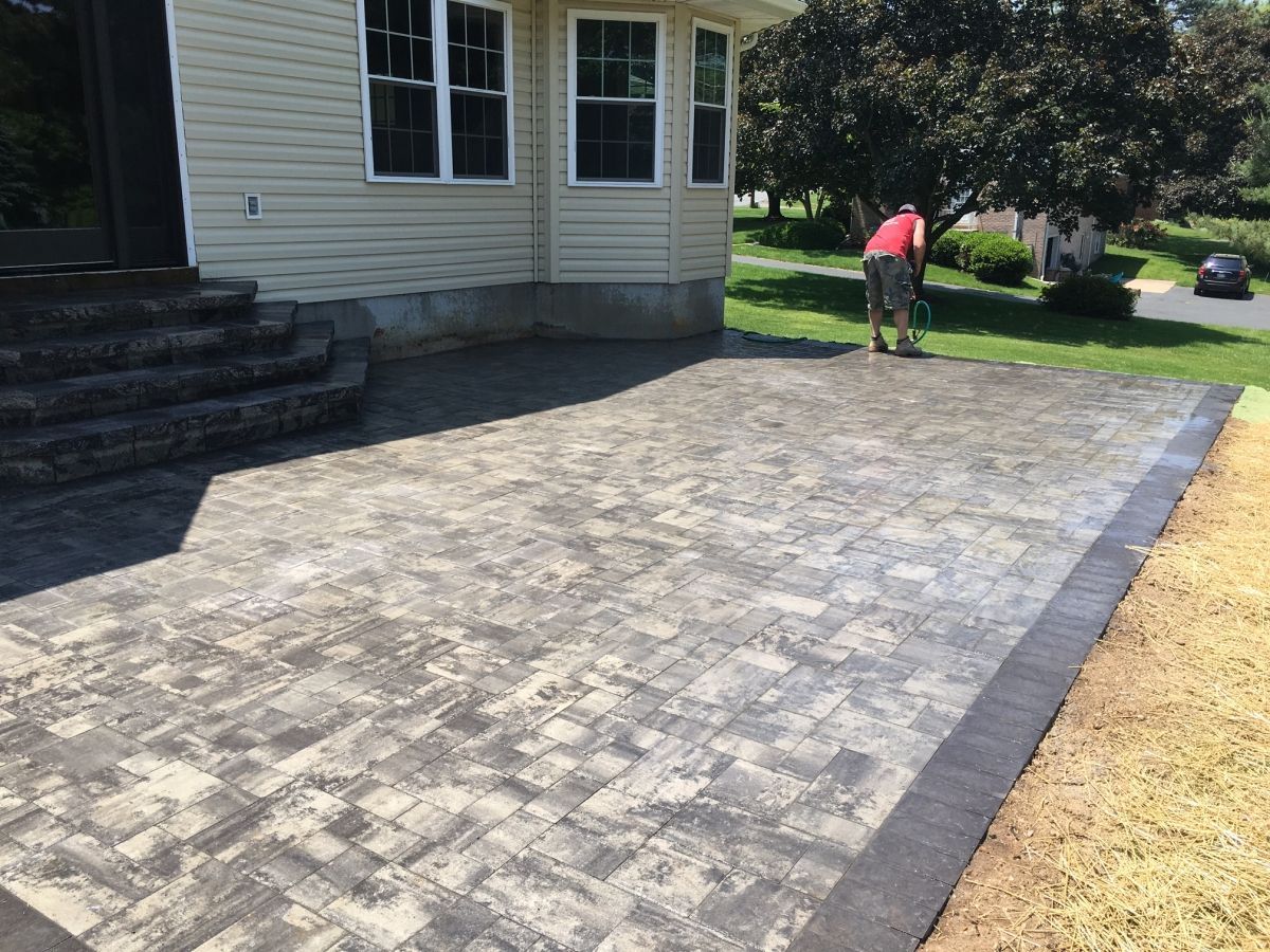 Paver patio beside a house, with a worker in a red shirt near the lawn.