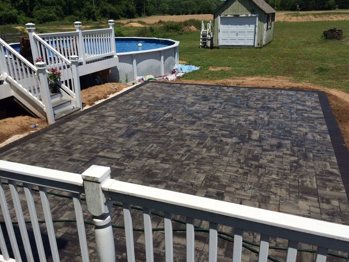 Backyard with an above-ground pool, white deck, and dark stone patio beside a grassy yard