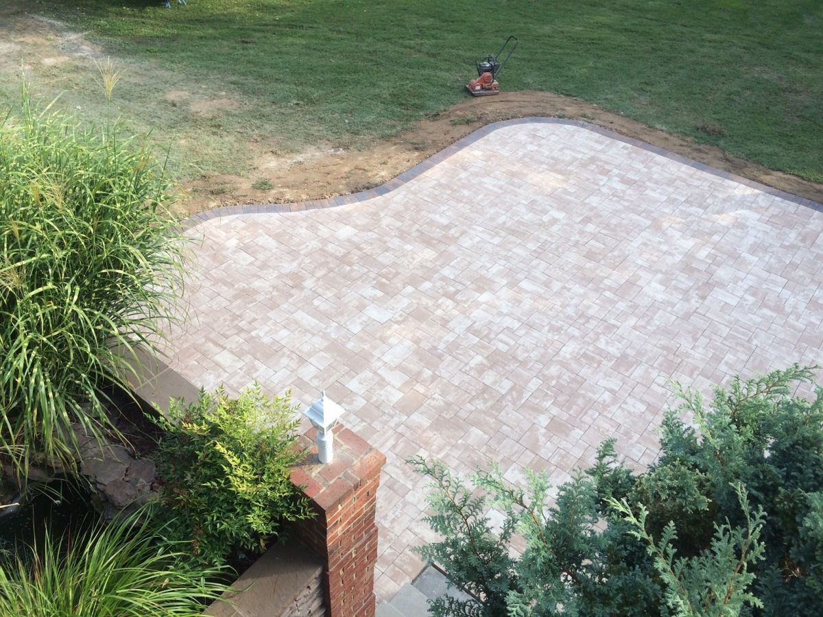 Backyard stone patio bordered by grass and shrubs, viewed from above