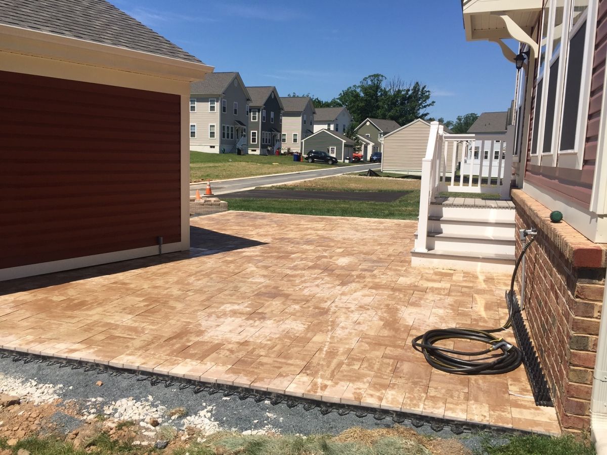 Backyard patio with a concrete slab beside a house, garage, and steps leading to a porch.