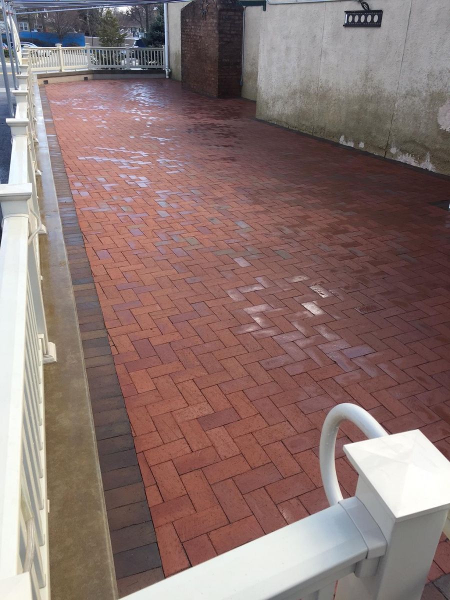 Red brick walkway beside a white railing and wall, wet from rain.