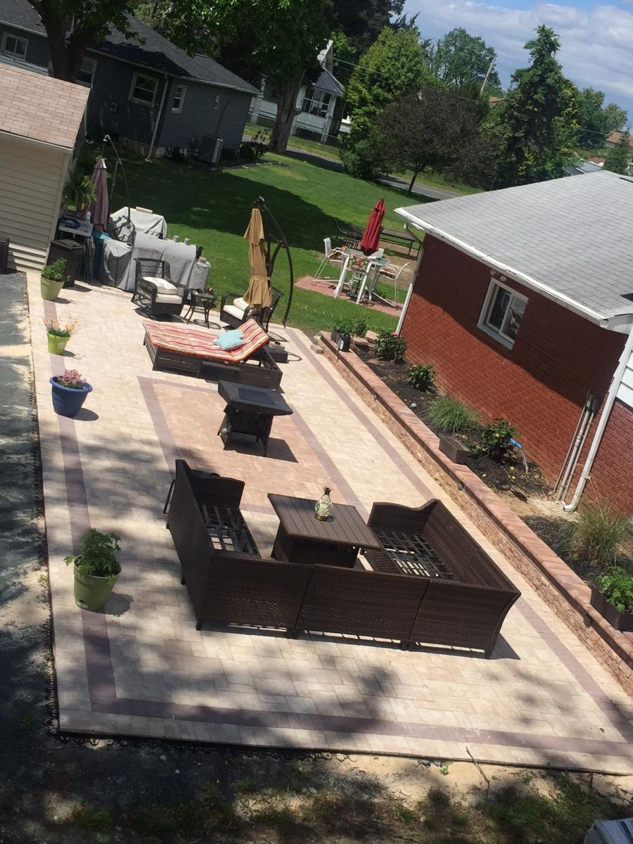 Backyard patio with outdoor seating, brick fire pit, and surrounding lawn beside a red house.
