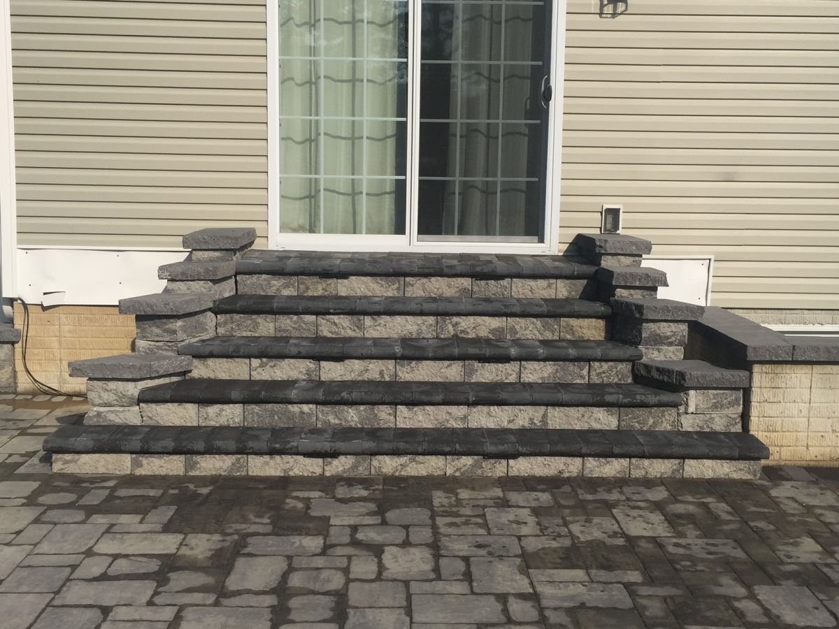 Stone front steps leading to a white house with a window and beige siding, surrounded by paved driveway.