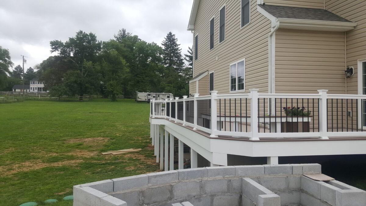 Backyard deck beside a tan house, with white railing and cinder blocks in the foreground