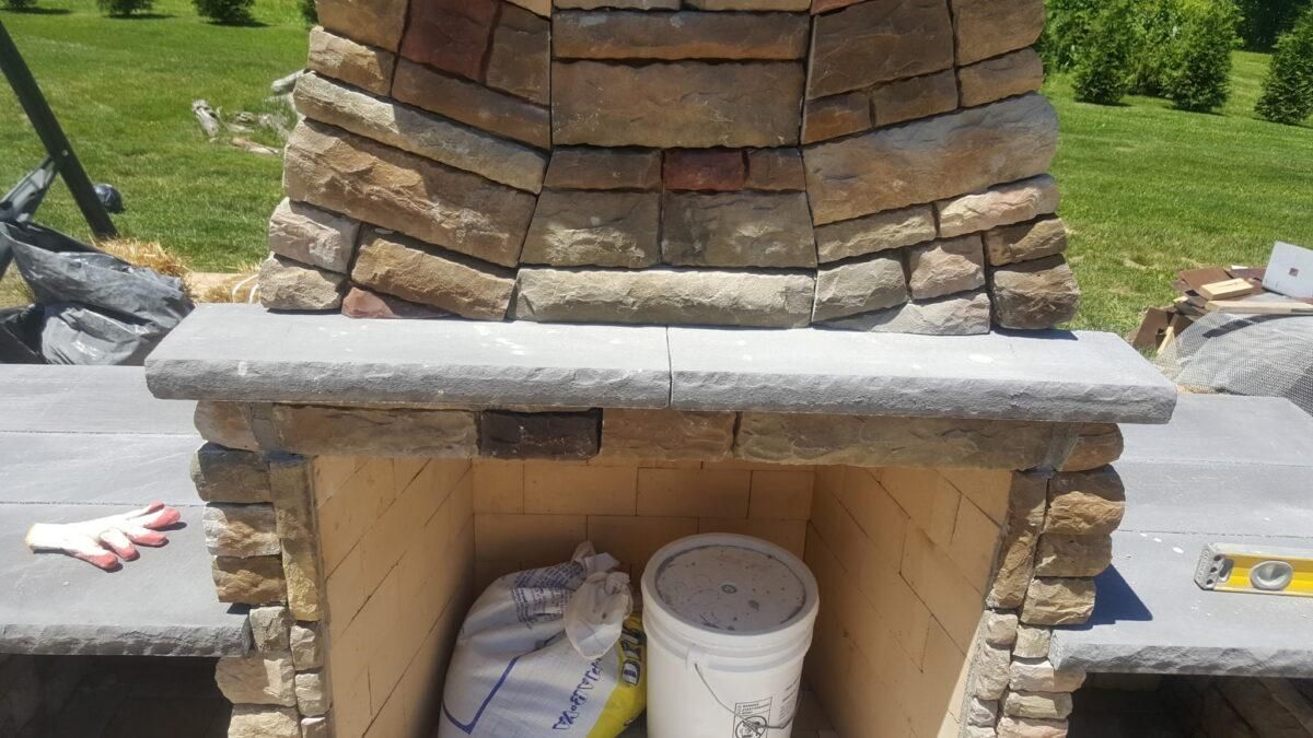 Stone outdoor fireplace under construction with a concrete mantel and buckets below
