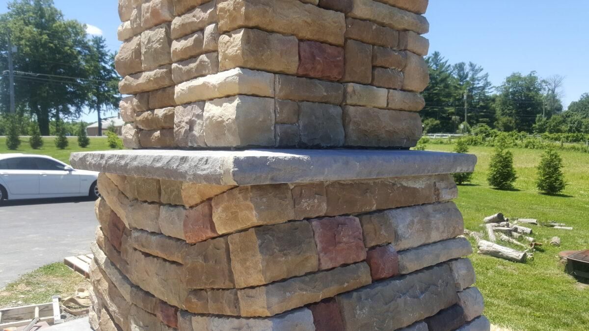 Stone pillar with stacked tan blocks and a white cap in a sunny grassy landscape