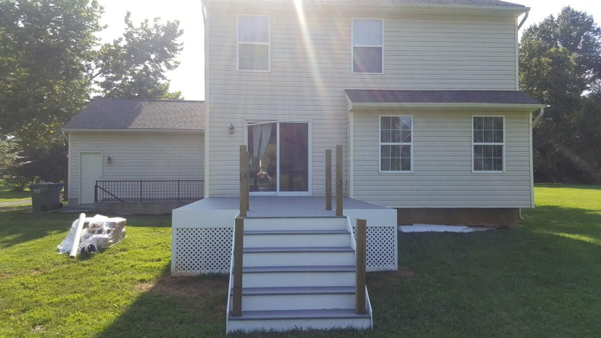 White two-story house with front porch steps, attached garage, and sunlit lawn