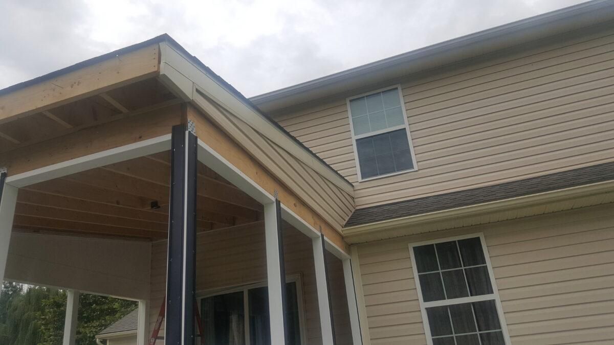 Covered porch with beige siding and white-trimmed windows on a two-story house