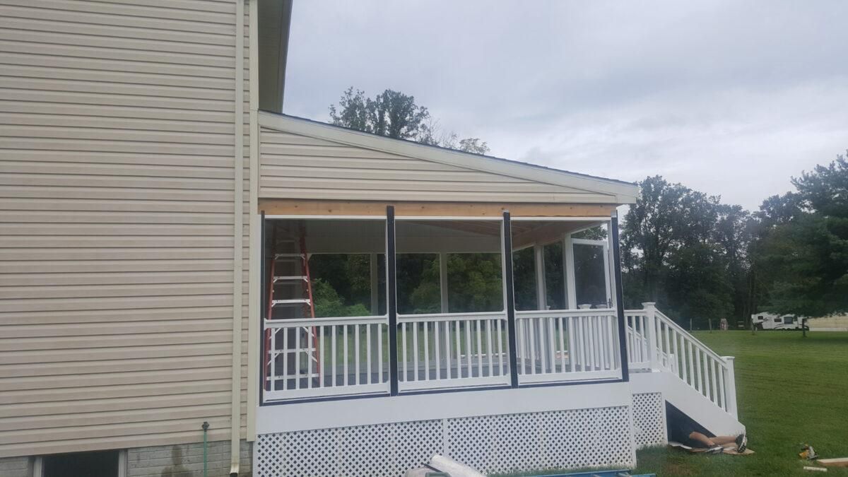 Covered porch with white railing and steps attached to a beige house on a cloudy day