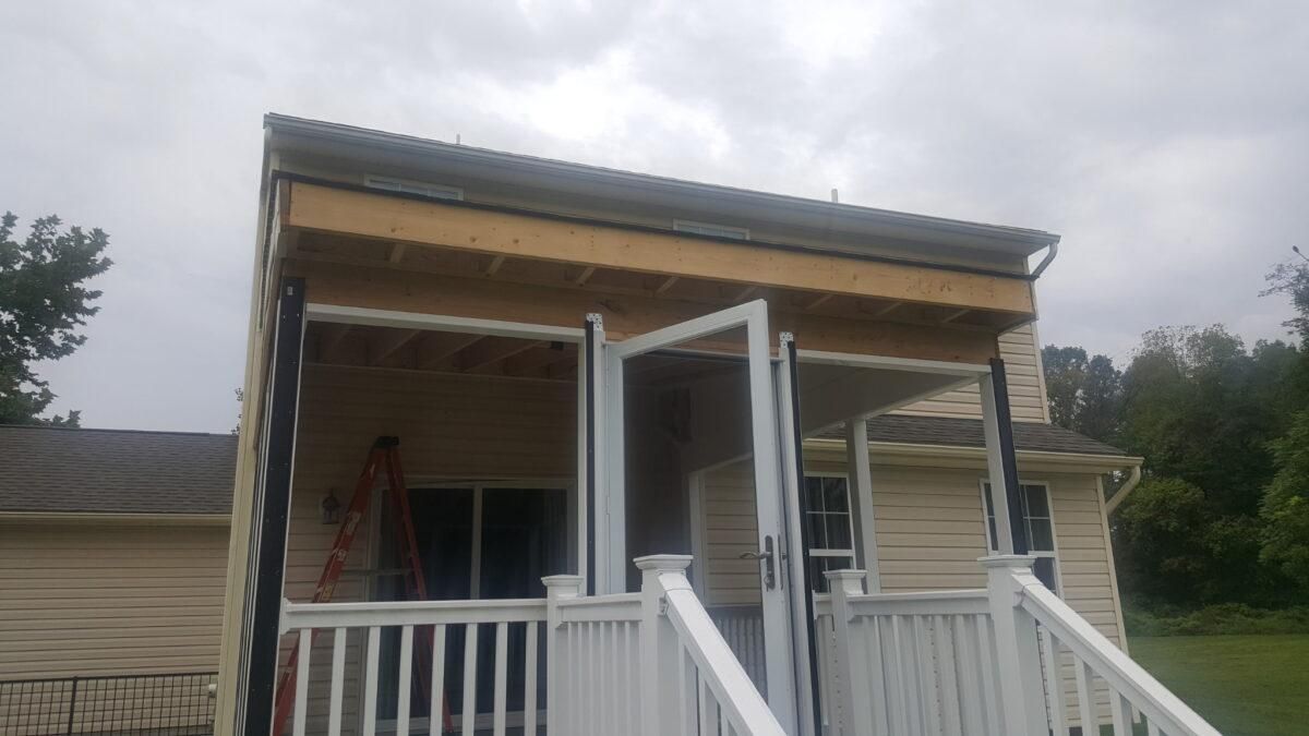 Small porch under construction with white railings and posts on a house, against a cloudy sky
