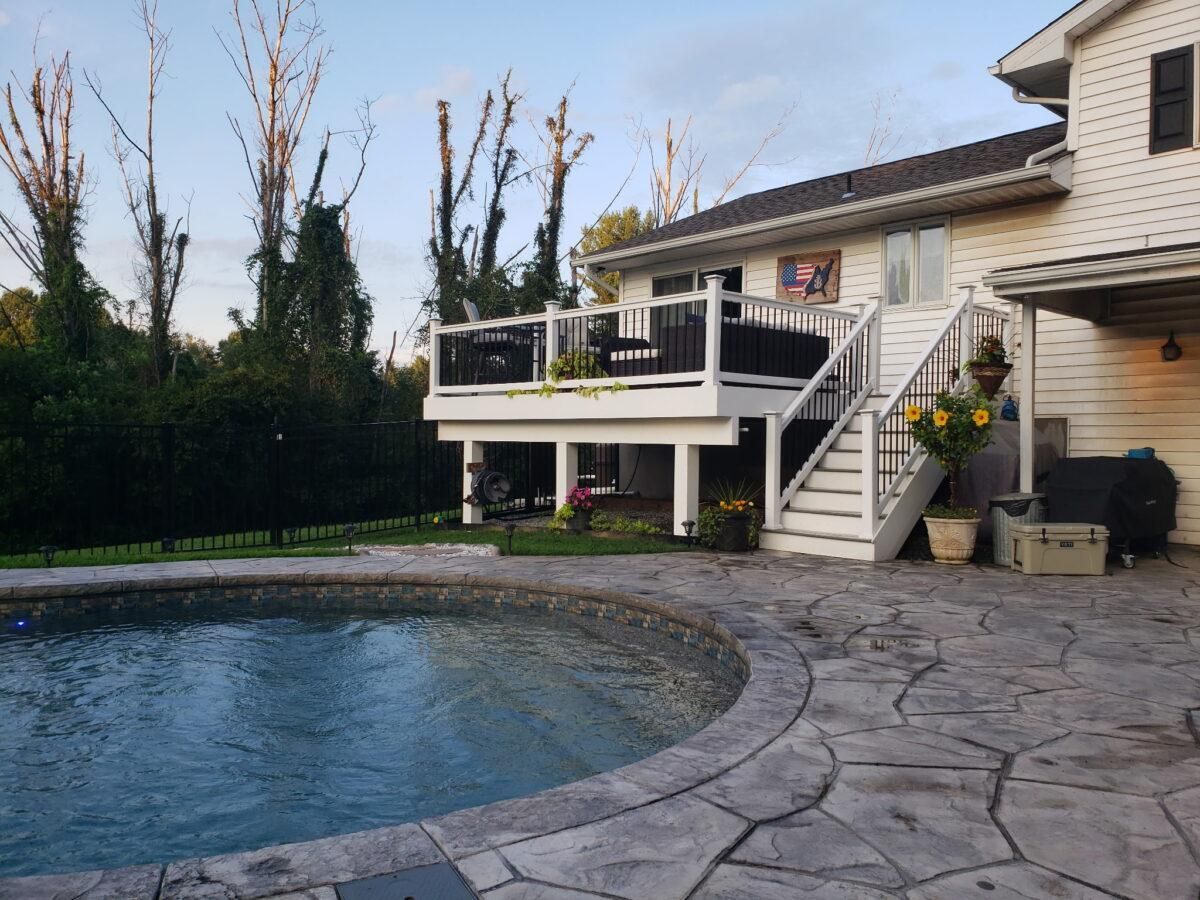 Backyard pool with stone patio and a house deck with stairs and potted plants