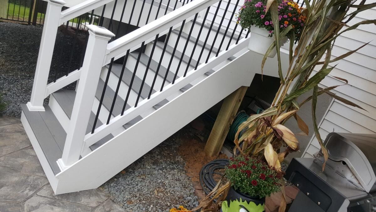 White wooden stairs with railing beside potted plants on a gravel patio