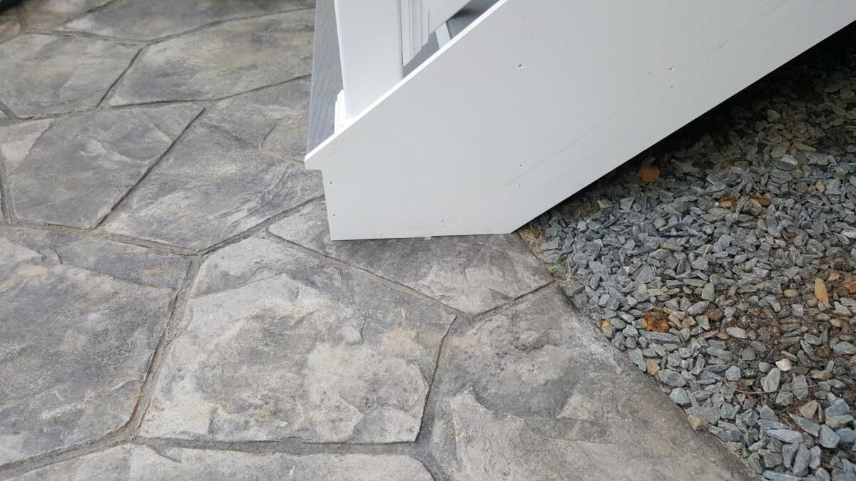 Stone patio beside a white stair or ramp, bordered by gravel.