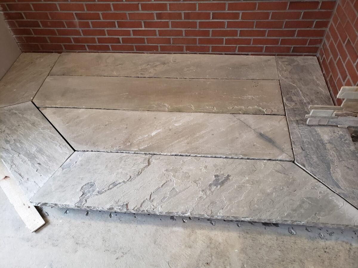 Cracked concrete walkway beside a red brick wall, with uneven, broken slabs.