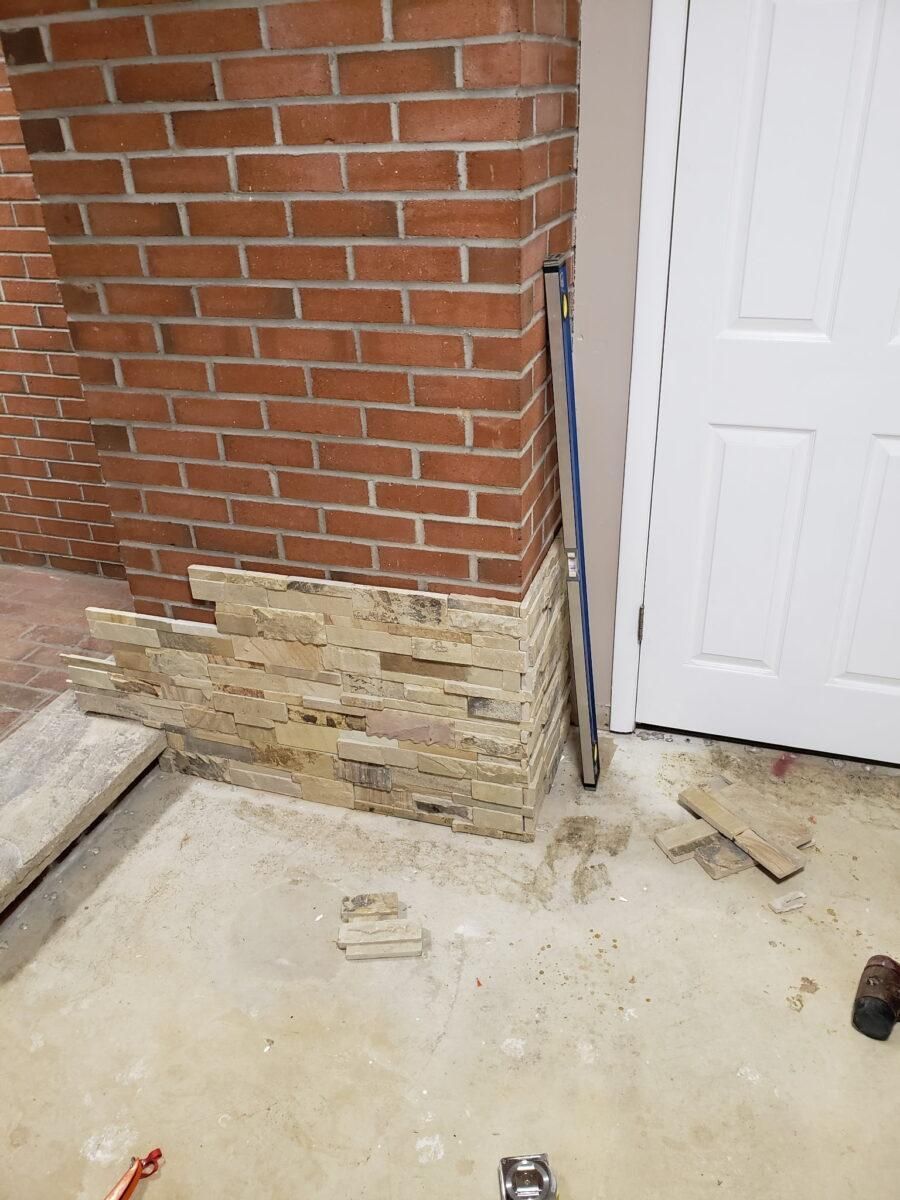 Partially exposed brick wall with damaged lower masonry and construction debris beside a white door