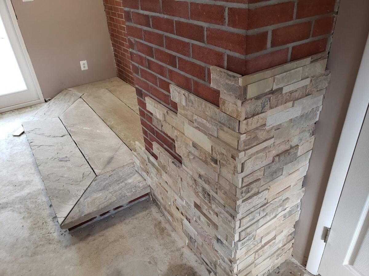 Interior wall with brick corner veneer and unfinished concrete floor, showing a raised patch near the base.