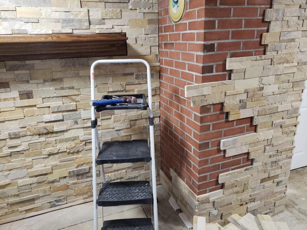 A white step ladder beside a brick column against a stone and brick wall.