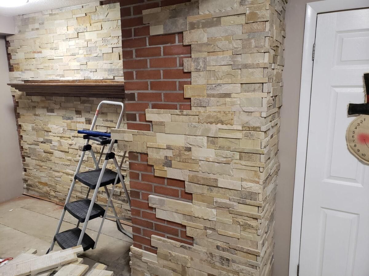 Partially covered interior wall with brick veneer, blue step ladder, and white door nearby