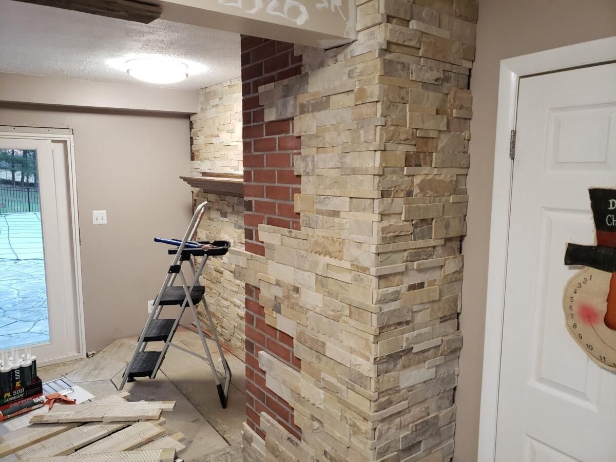 Living room with stacked stone fireplace, ladder, and partially painted walls underway.