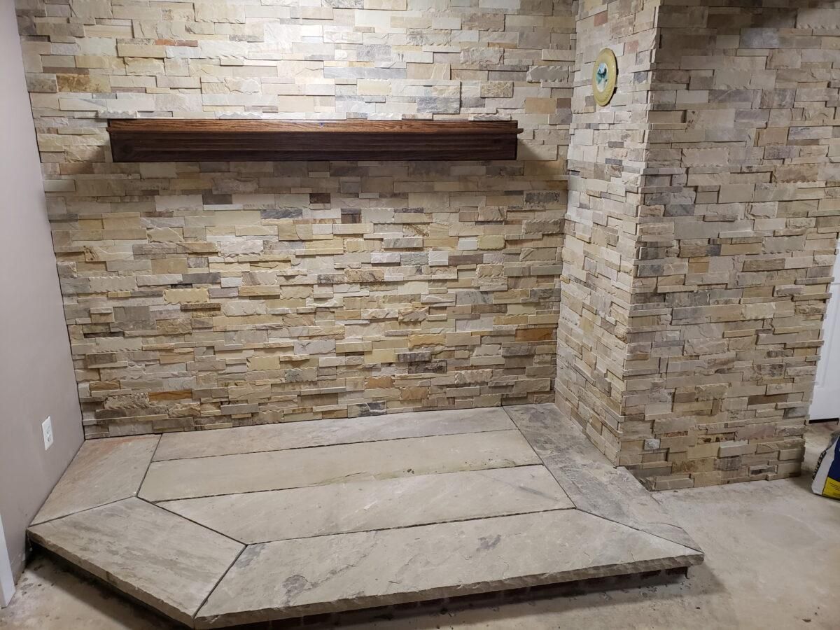 Empty fireplace area with stone wall, wooden mantel, and a raised stone hearth platform