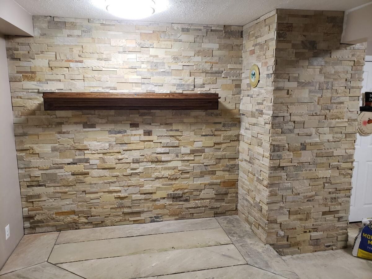 Empty room with stone accent wall, dark shelf, and tiled floor under ceiling lights