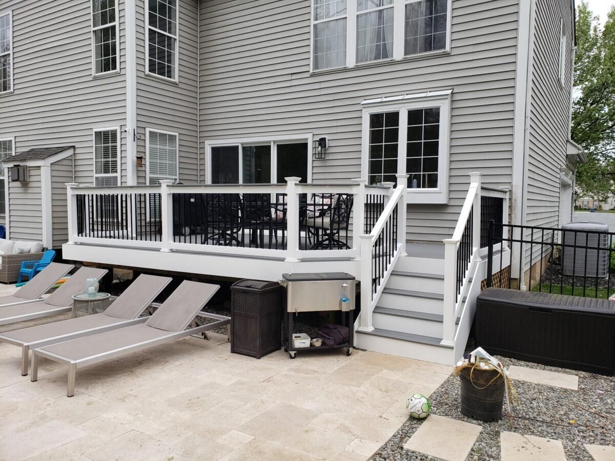 Back patio deck with white railing, stairs, and lounge chairs beside a gray house