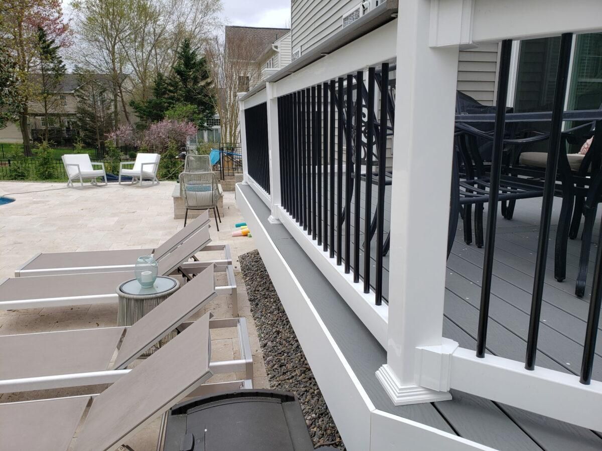 Outdoor patio with white lounge chairs beside a black-and-white deck railing and gravel border