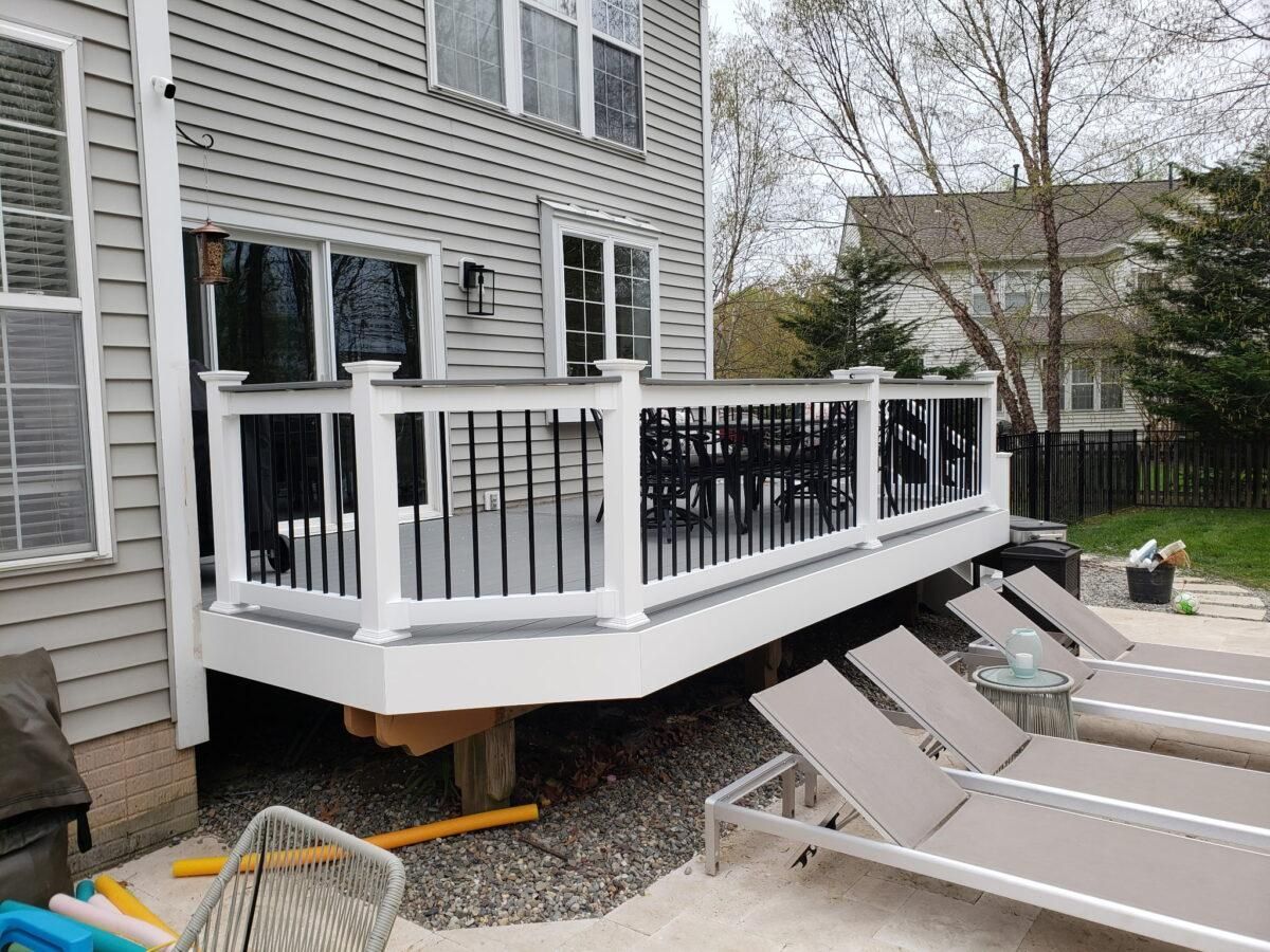 White-railed backyard deck attached to a house beside outdoor lounge chairs and gravel.