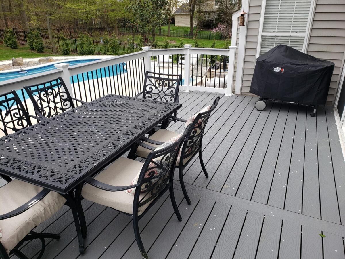 Poolside deck with black patio table and chairs, gray boards, white railing, and covered grill