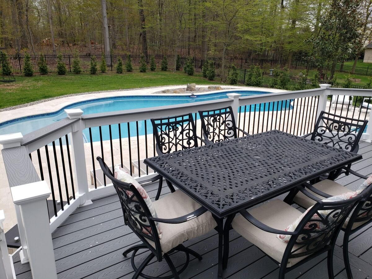 Patio dining set beside a fenced backyard pool with lounge chairs and trees beyond