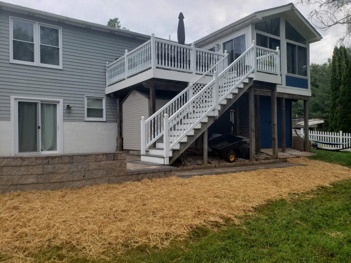 Two-story gray house with white deck stairs and a covered patio over gravel yard