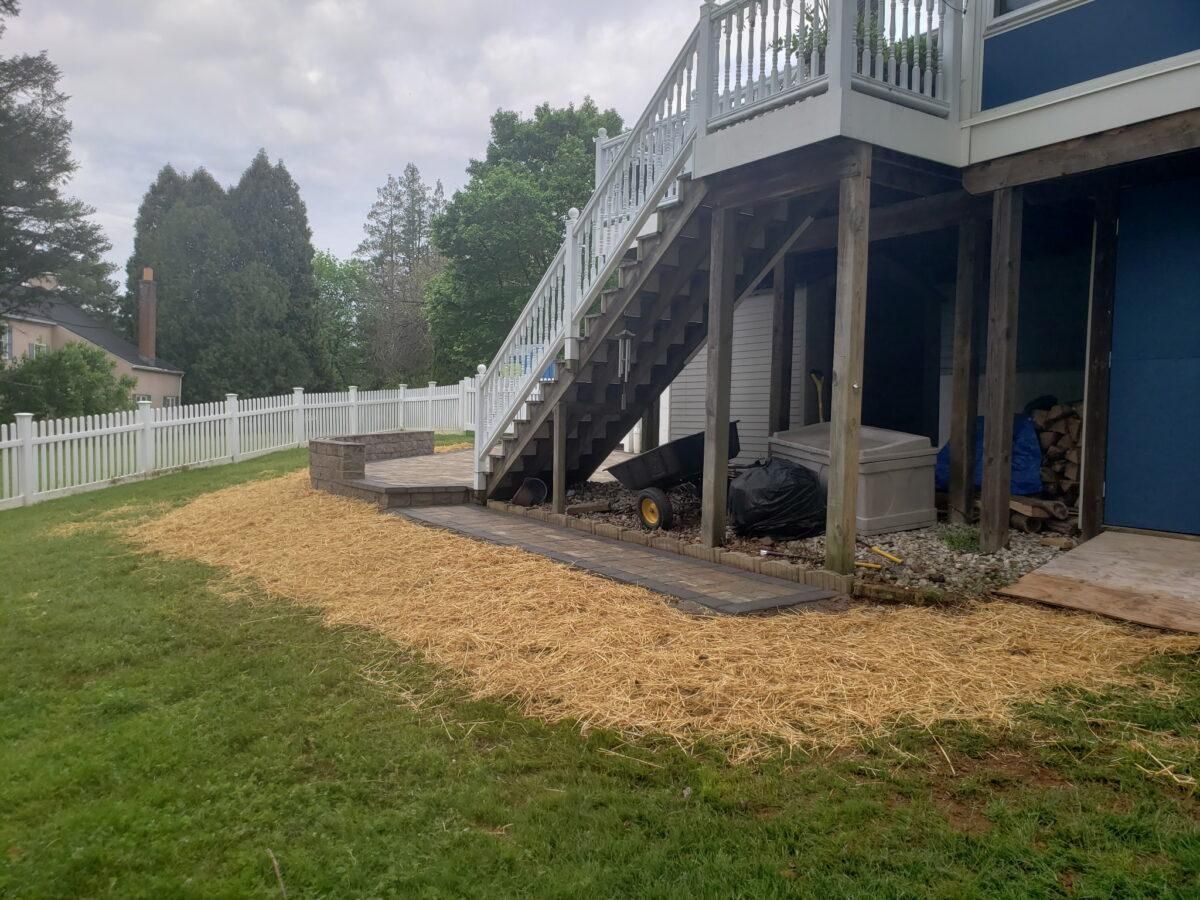 Backyard with white fence, sloped lawn, and elevated deck stairs beside a house