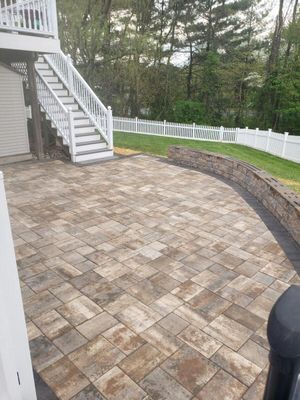Stone-paver patio beside white stairs and fence in a wooded backyard