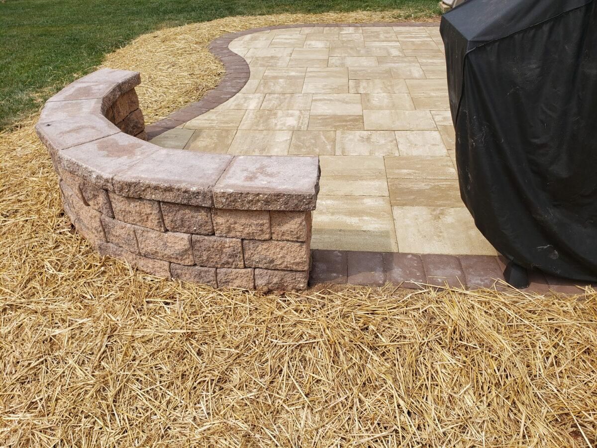 Curved stone garden wall edging a paved patio beside mulch and covered furniture