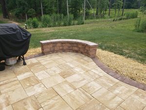 Stone patio with curved brick retaining wall beside a grassy yard and grill