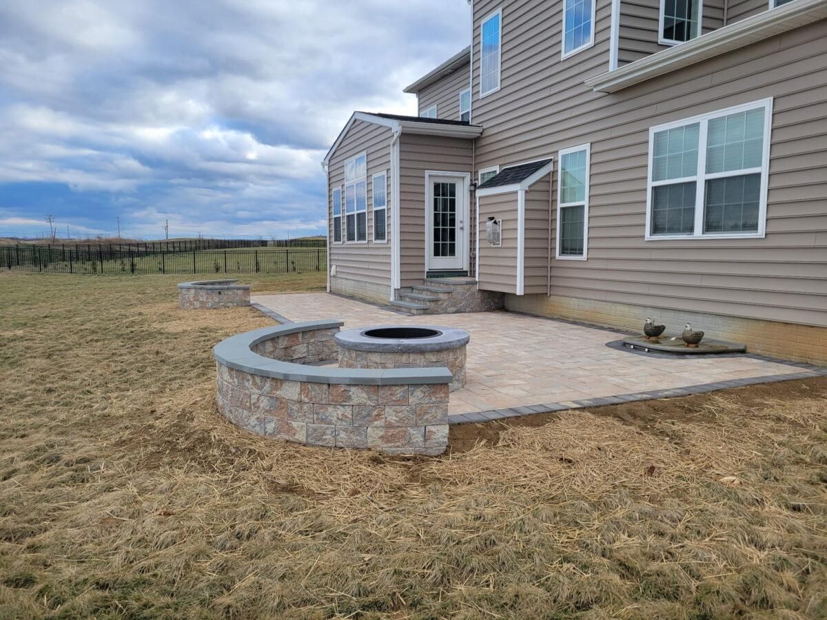 Backyard patio with stone fire pit, tan house exterior, and open field in the background