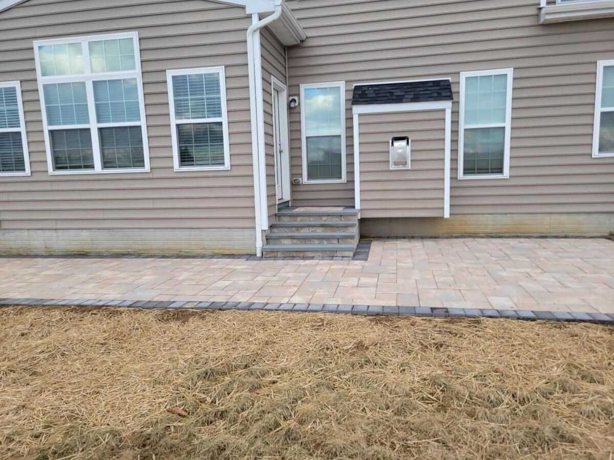 Back patio with stone pavers, steps, and beige house siding and windows