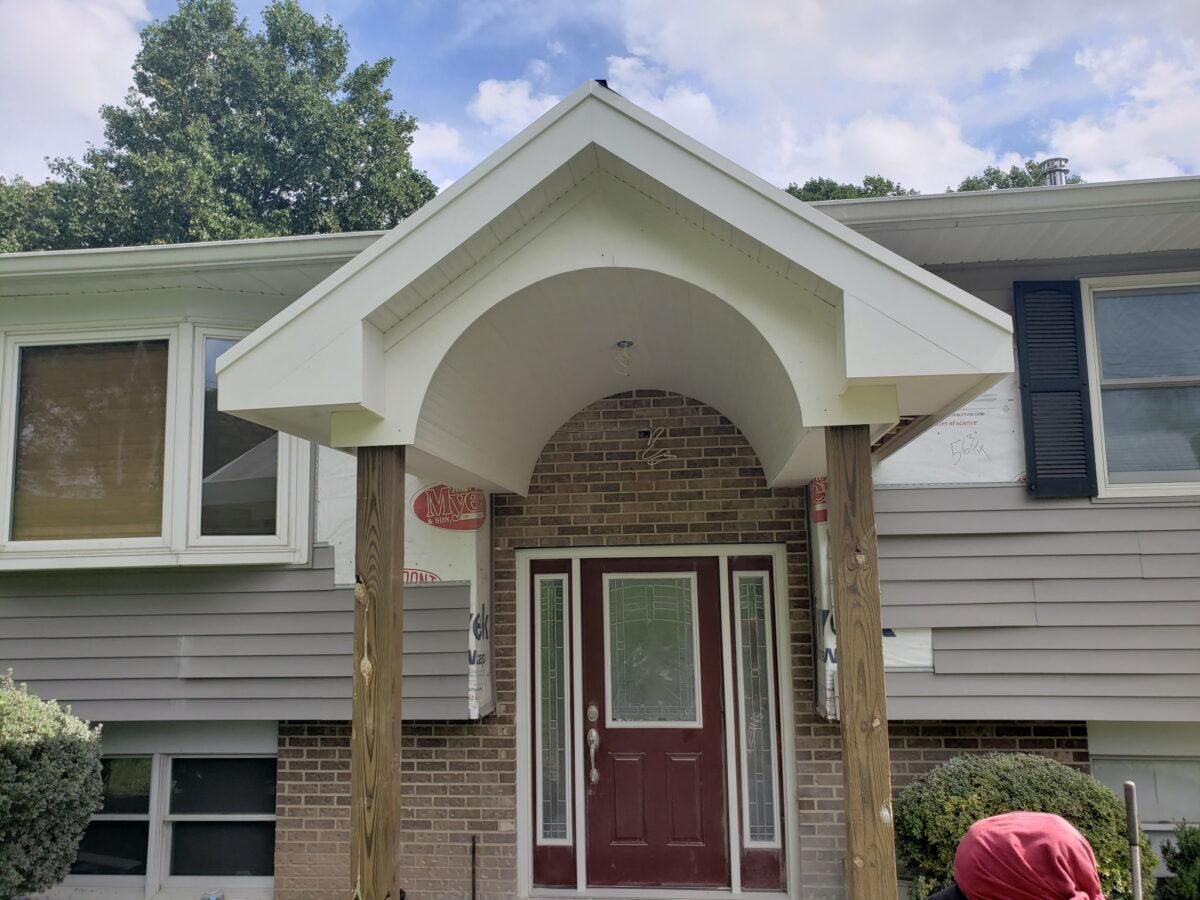Front entrance of a house with white trim, brick archway, and a red front door