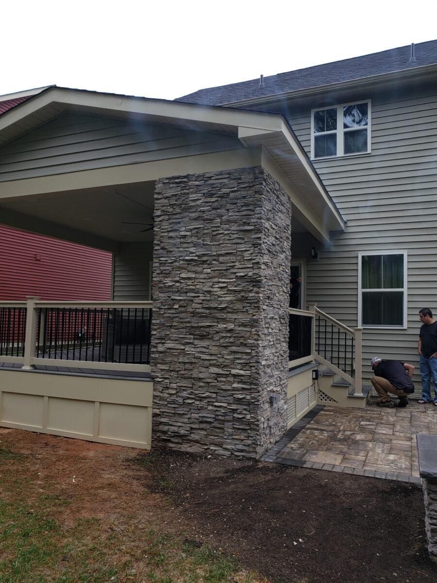 Covered porch with stone column beside a beige house and small patio walkway.