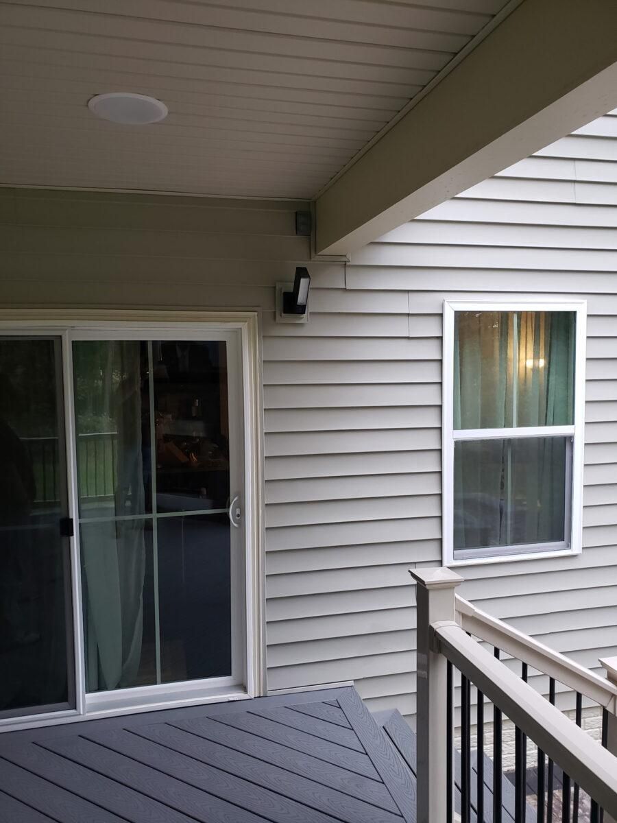 Covered porch with gray siding, a sliding glass door, a window, and a railing.