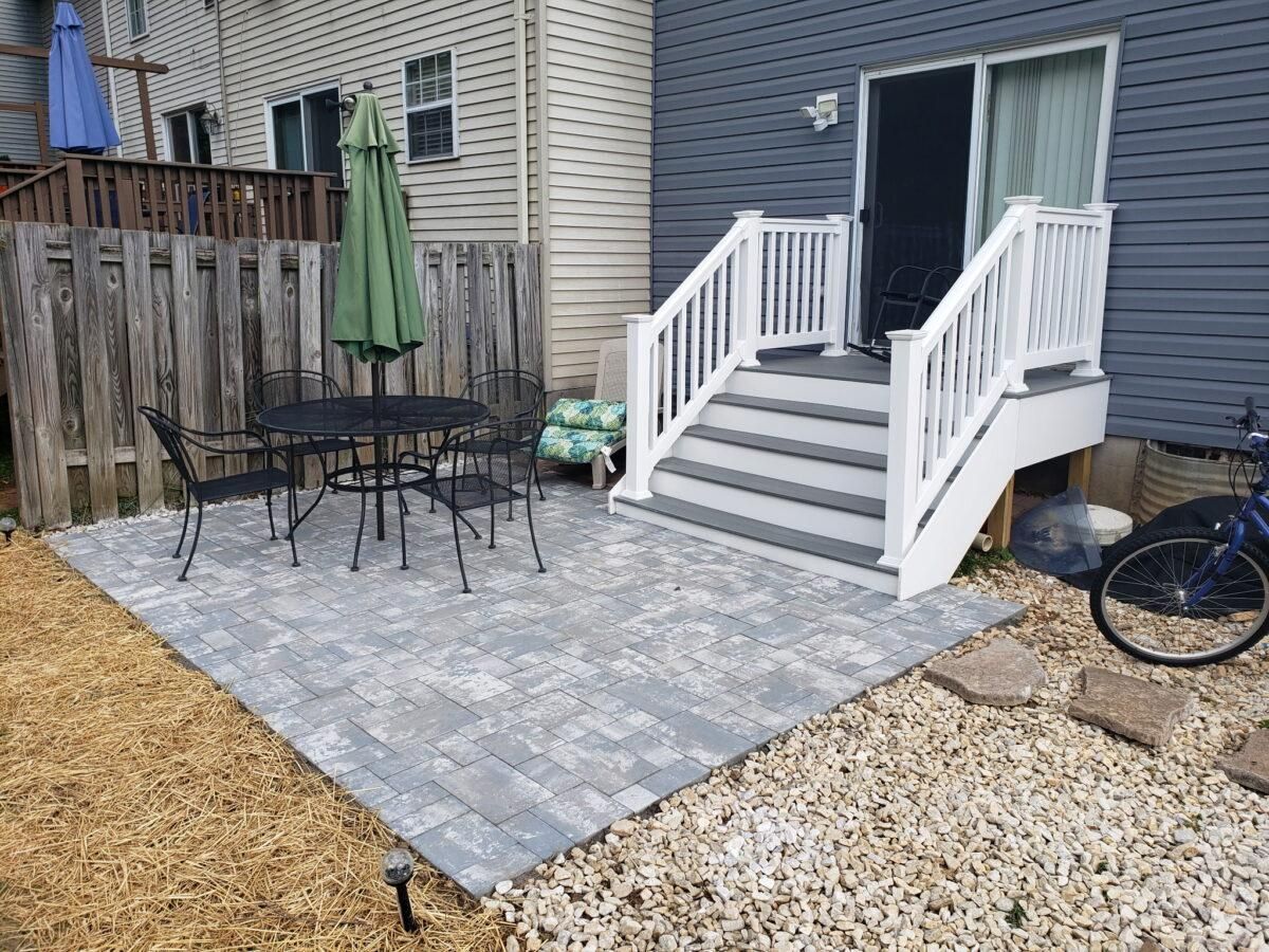 Backyard patio with gray stone pavers, black table and chairs, and white steps to a sliding door