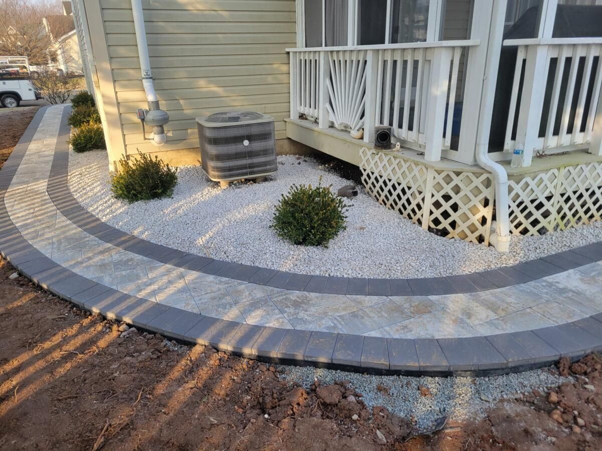 Curved concrete walkway with white gravel landscaping beside a porch and yellow house exterior.