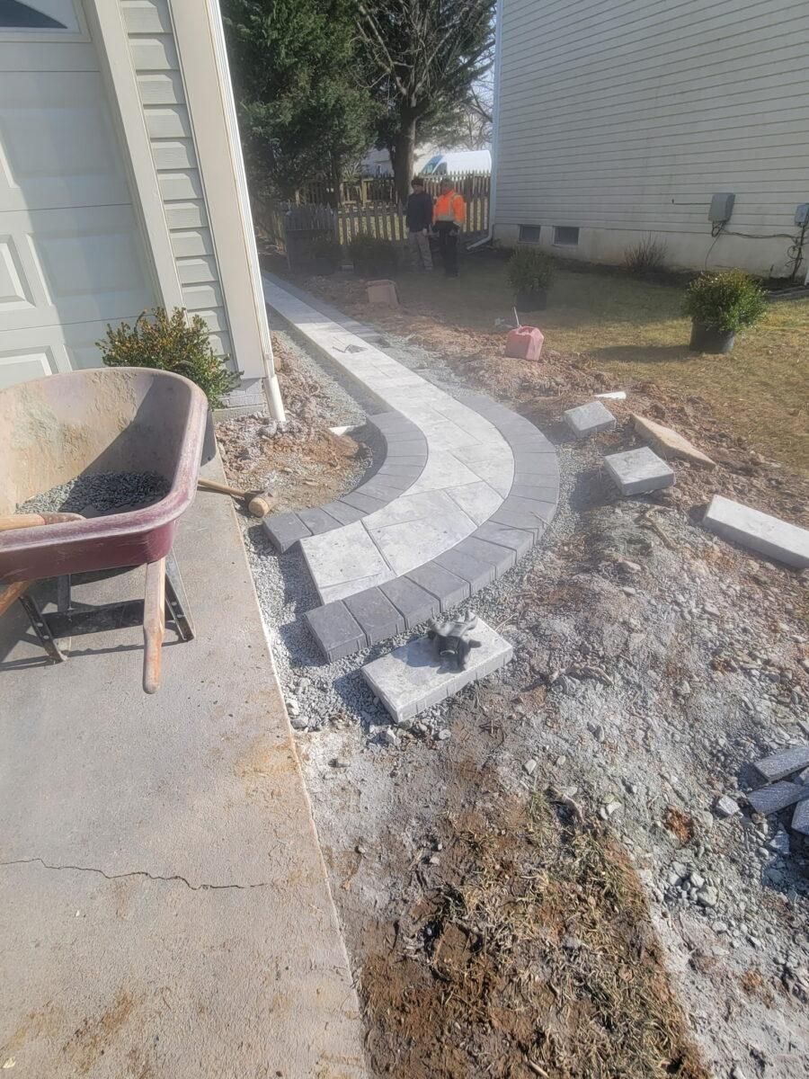 Curved stone walkway under construction beside a house, with gravel, tools, and unfinished edging
