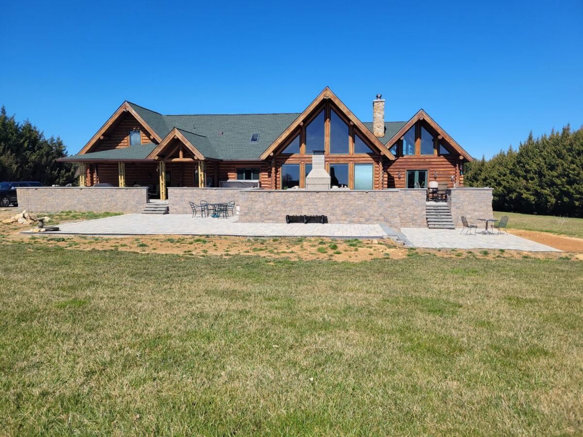 Large modern log house with stone steps and a broad grassy lawn under a clear blue sky