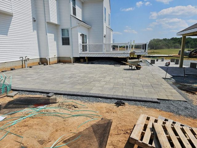 Backyard patio under construction beside a white house, with paving stones and construction materials.