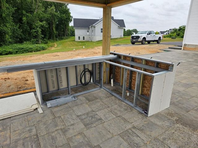 Outdoor kitchen/bar under construction with metal framing, paver floor, and a white truck in the background