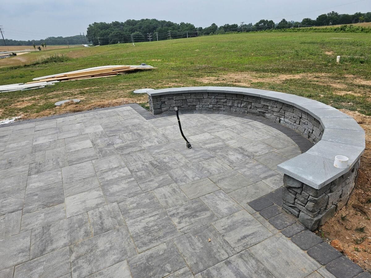 Curved stone patio bench with fire pit in a grassy outdoor yard
